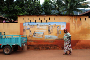 A woman in Togo walks past a painted sign about the dangers of HIV. Public health researchers and practitioners from around the world will meet in South Africa in September to discuss how to accelerate progress toward ending HIV as a public health threat, at a conference co-chaired by WashU faculty. (Photo credit: Getty Images)